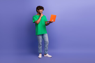 Positive man holding orange laptop smiling against purple backdrop showcasing stylish casual fashion and positive energy