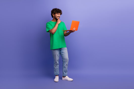 Positive man holding orange laptop smiling against purple backdrop showcasing stylish casual fashion and positive energy - Powered by Adobe
