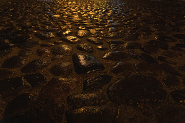 Wet cobblestone street illuminated by warm night lights – close-up texture of old stone pavement after rain, glistening reflections in darkness