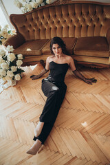 Elegant woman in black dress resting on floor by sofa