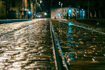 Wet cobblestone tram tracks at night with city lights reflections after rain – urban street perspective
