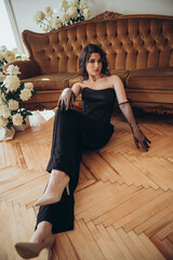 Elegant model in black dress sitting beside sofa