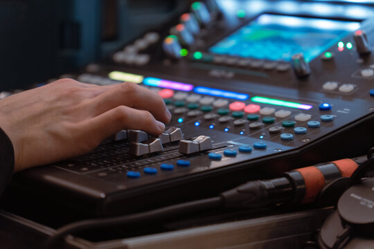 Sound engineer adjusting audio mixing console with colorful lights and controls in studio or live concert setup