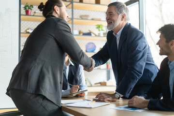 Happy business men executive partners making agreement with handshake at team meeting