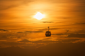 Cable car at sunset with the sun behind and orange-hued clouds