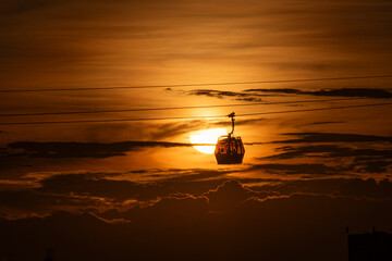 Cable car at sunset with the sun behind and orange-hued clouds