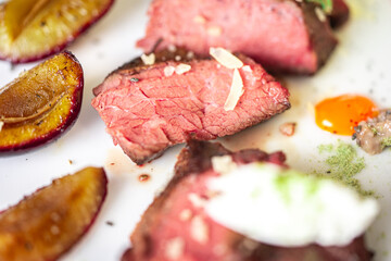 Medium-rare steak, sliced, with dogwood sauce on a white plate with roasted plums and rosemary cream cheese dumplings. Top view.