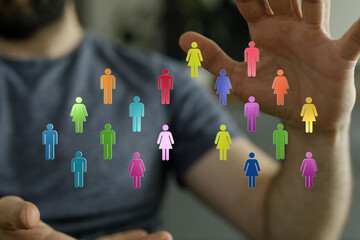 Image of colorful human figures, representing diversity, held in a hand. Illustrating teamwork,...