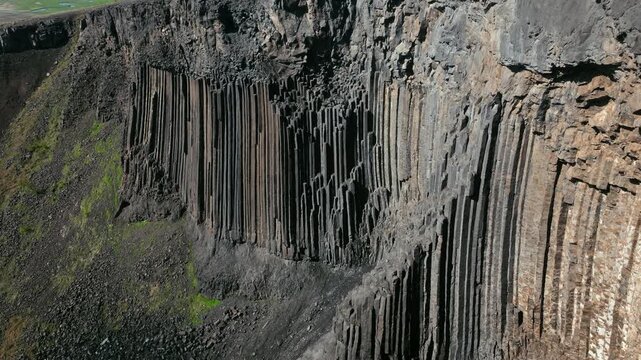 Close aerial view of basalt formations near Hengifoss waterfall in East Iceland. The drone captures the rugged cliff textures in sunlight.