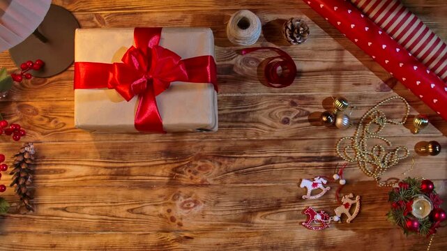 Top view of women hands stacking Christmas gifts with red bows and a Merry Christmas card on a wooden table. Festive packaging with decorations, handmade.