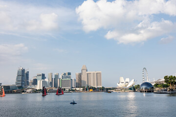 View of modern buildings and architecture, including the ArtScience Museum, line the waterfront under a sky dotted with fluffy clouds, Singapore, Singapore.