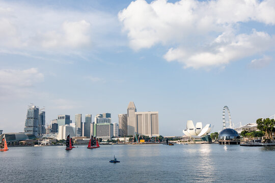 View of modern buildings and architecture, including the ArtScience Museum, line the waterfront under a sky dotted with fluffy clouds, Singapore, Singapore.