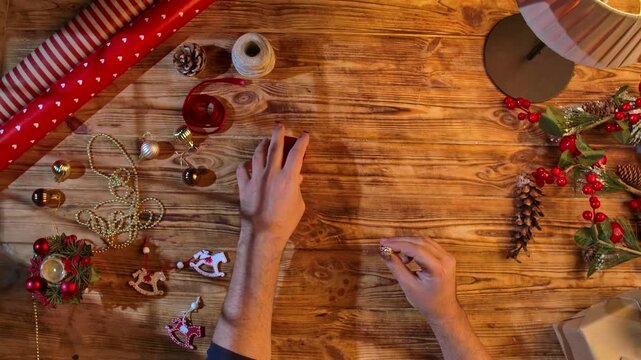 Top view of a man hands preparing gifts and placing an engagement ring in a red box. Festive packaging with decorations, handmade.