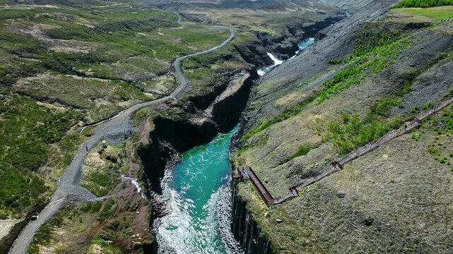 Stu&eth;lagil Canyon with viewing platform and turquoise river in East Iceland. Tourists walk along the elevated wooden platform above Litlanesfoss canyon near Hengifoss waterfall in East Iceland.