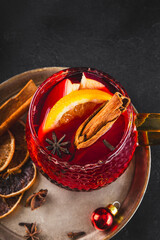 Holiday Mulled Wine with Orange and Apple in glass Mug Surrounded by Christmas Decor on black background vertical photo