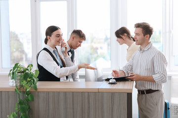 Receptionist and hostess working with guests at reception desk in hotel