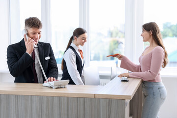 Receptionist and hostess working with guest at reception desk indoors, selective focus