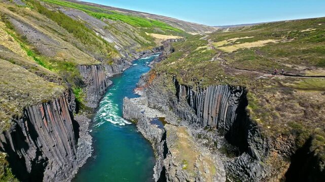 Aerial shot of Stu&eth;lagil Canyon in East Iceland. The drone captures the turquoise glacial river winding between tall volcanic cliffs.