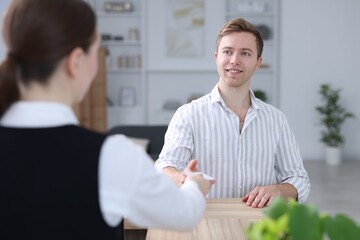 Receptionist giving hotel key card to guest at reception desk indoors, selective focus