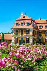 Panoramic view of Rajec Jestrebi Chateau on a sunny summer day with blue sky, blooming pink roses, and a fountain in front of the historical building.