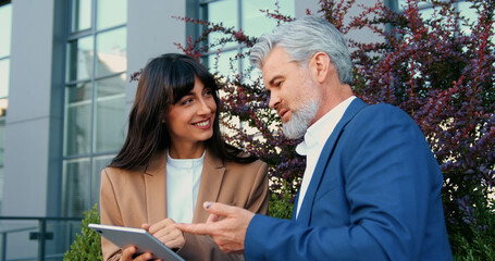 Close-up of a young woman smiling and holding a tablet while an older man is talking and looking at the tablet screen during a business conversation