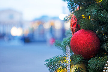 Red ball on Christmas tree on background of city street. Street is out of focus. Place for advertising. Background for Christmas card.