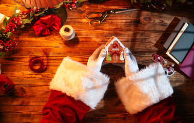 Top view of Santa's gloved hands creating festive decorations with paint, ribbons, and scissors...