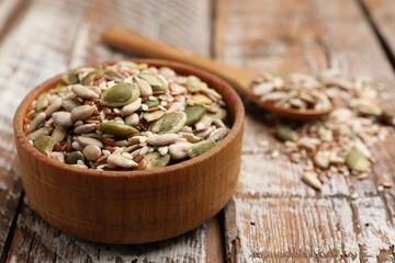 Mix of seeds in bowl and spoon on wooden table, closeup