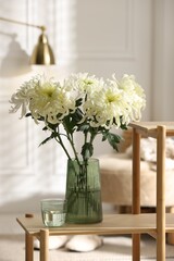 Beautiful white chrysanthemum flowers in vase on wooden shelf indoors