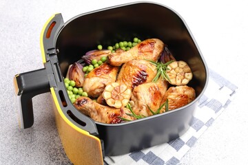 Air fryer basket with grilled chicken drumsticks, spices and green peas on grey table, closeup