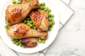 Grilled chicken drumsticks, green peas and onion on white marble table, top view. Space for text