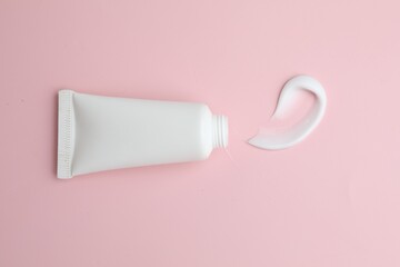 Sample of moisturizing cream and tube on pink background, top view