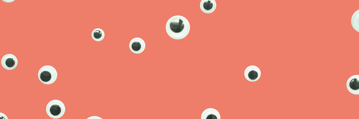Scattered googly eyes on coral background creating a playful and surreal effect.
