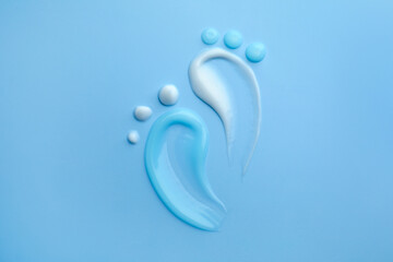 Feet shape made of samples of different cosmetic products on light blue background, flat lay