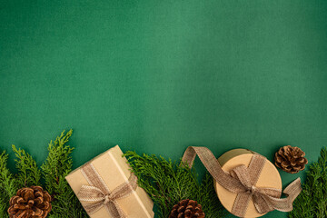 Natural holiday flat lay with kraft-wrapped gifts, pine cones, greenery, and wooden snowflakes on a green background.