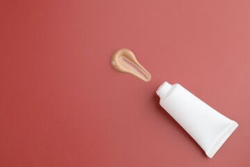 Tube with foundation on red background, top view. Space for text