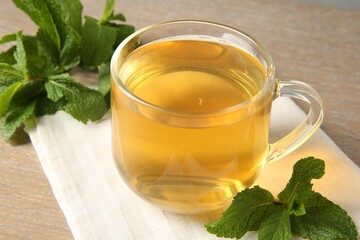 Cup of delicious tea and mint on wooden table, closeup