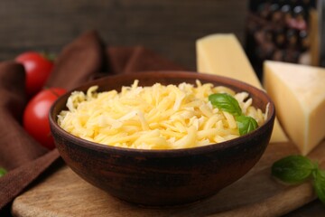 Grated and pieces of cheese with basil on wooden table, closeup