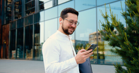 Side view of close up male hands using smartphone and holding laptop. Fingers hands dialing number...
