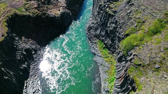 Wide drone view of Stu&eth;lagil Canyon in East Iceland. The river flows through a dramatic landscape of cliffs and mossy slopes.