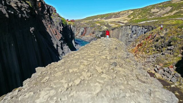 Drone footage of tourist exploring Stu&eth;lagil Canyon in East Iceland. The visitor walks along rocky cliffs above the turquoise river.