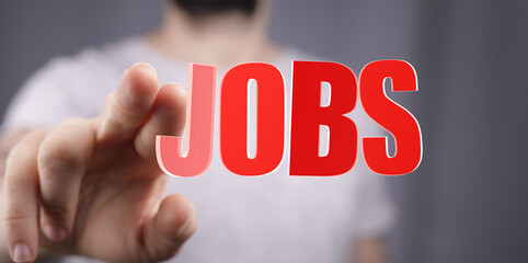 Hand reaching toward the word JOBS, signifying employment, hiring, and career opportunity. Concept of job search and career development.