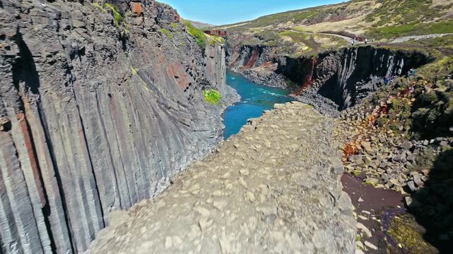 Aerial shot of Stu&eth;lagil Canyon in East Iceland. The narrow turquoise river winds through hexagonal basalt columns in sunlight.