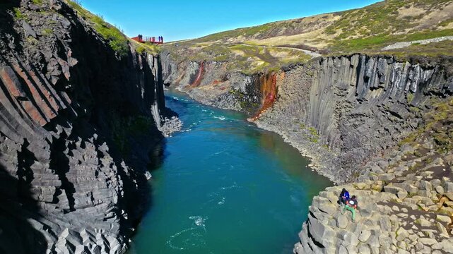 Female tourist walking along basalt cliffs in Stu&eth;lagil Canyon, East Iceland. The explorer enjoys panoramic views of the turquoise river below.
