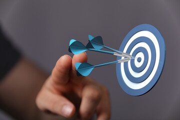 Close-up of a hand pointing to a dartboard with three darts hitting the center. Represents successful business, goals and achievement, focus, ta