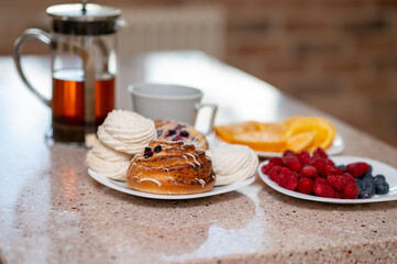 Teapot, marshmallows, buns and fruits on a kitchen countertop in morning light