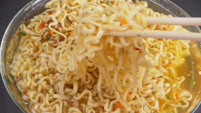 Stirring Instant noodles with Asian chopsticks in glass pot, close up