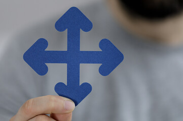 Close up of a hand holding a blue arrow showing a concept of multiple directions, making a choice, or options.