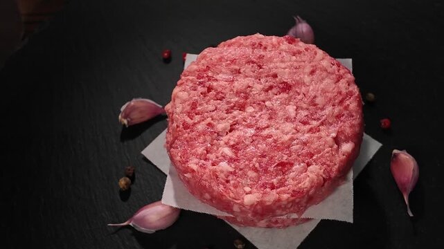 raw ground beef burger patties separated by parchment paper decorated thyme, garlic on slate black background, concept of vibrant colors for cooking inspiration, close up, rotation