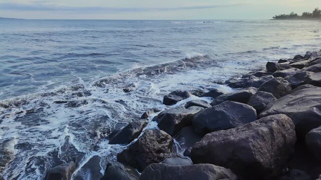 Black volcanic stones on Bali, Indonesia coastline create stunning contrast with crashing waves under sundown sky, showcasing natures power and beauty in harmony